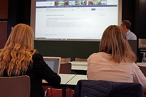 Zwei Studierende mit Laptop sitzen mit dem Rücken zur Kamera in einem Hörsaal während der Langen Nacht der Hausarbeiten 