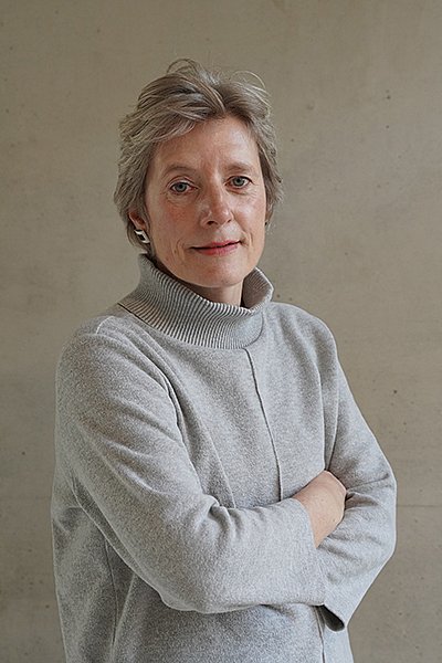 Prof. Dr. Kerstin Bremser in einem eleganten grauen Rollkragenpullover vor grauem Hintergrund