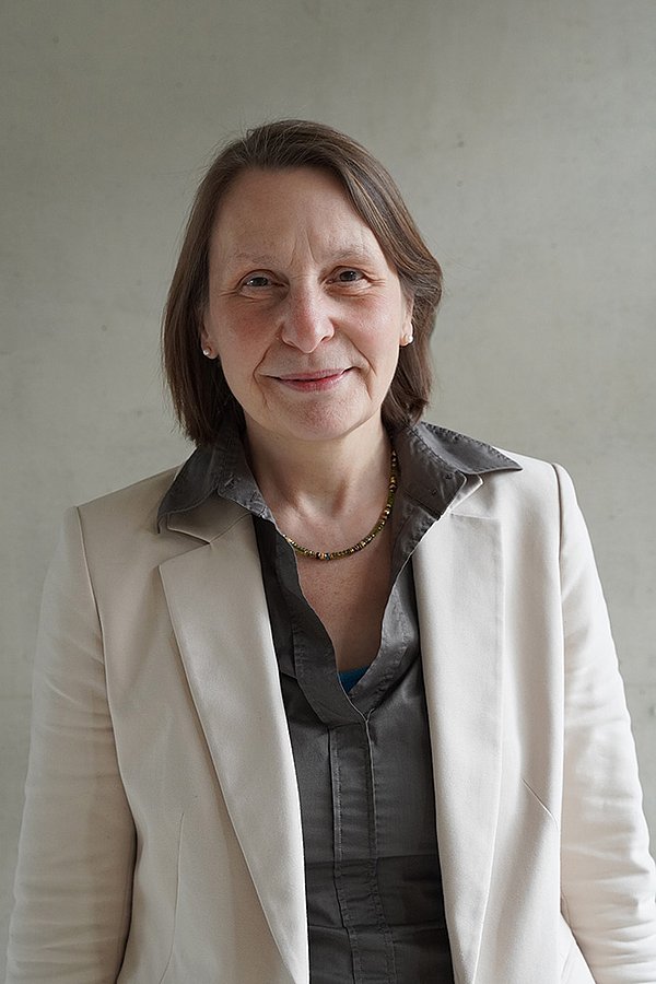 Prof. Dr. Elke Theobald wearing a grey blouse and a white blazer against a grey background