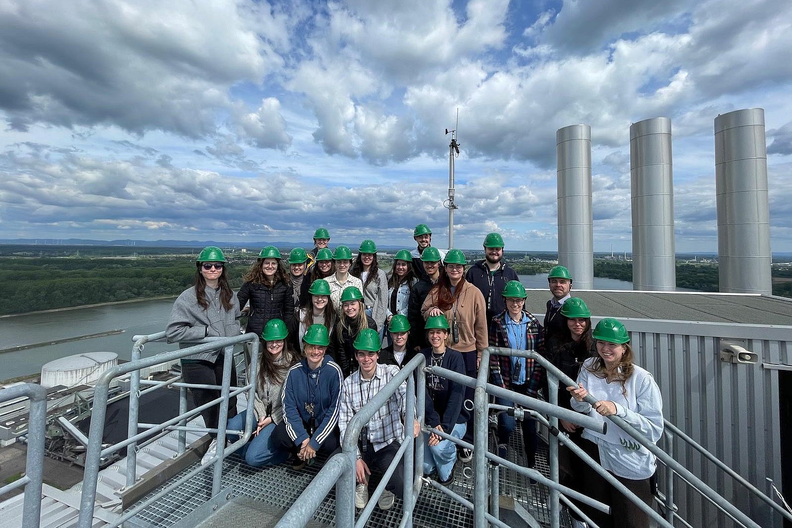 Gruppenbild mit grünen Helmen auf Dach einer Industrieanlage mit Schornsteinen