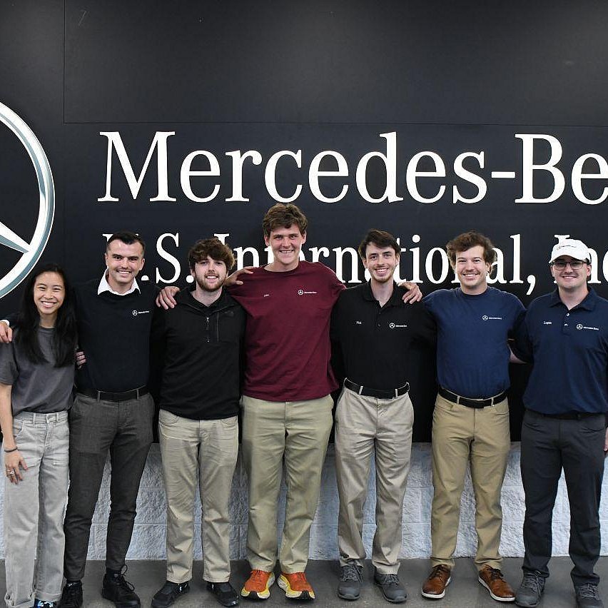 Sieben Mitarbeiter von Mercedes-Benz United States International, Incorporated vor einem Mercedes Benz-Hintergrund 