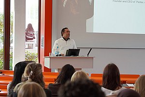 Gunjan Bhardwaj, Alumnus der Business School Pforzheim und heutiger CEO von Partex.AI N.V., hält in einem weißen Pullover am Pult des Hörsaals eine Rede vor Bachelor-Studierenden