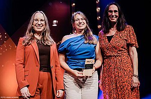 Anja Körnle, Alumna des Studiengangs Corporate Communication Management, strahlt bei der Verleihung des BdKom Talent Awards 2026 in einem blauen Oberteil in die Kamera