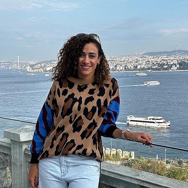 Alumna Yousra Emara aus Ägypten lehnt entspannt an einem Geländer an einem See