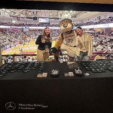A student stands next to a mascot at a merchandise stand during a football game.