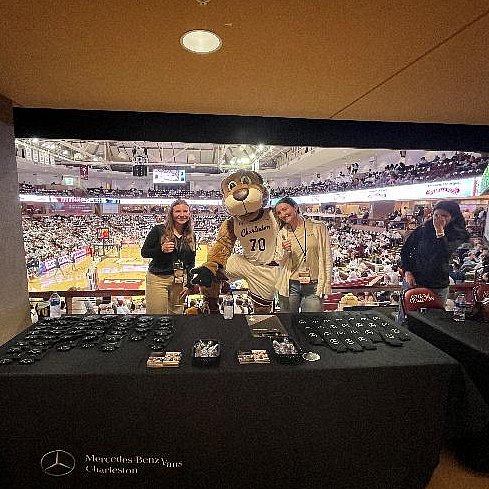 Studentin steht an einem Merchandise-Stand bei einem Footballspiel neben einem Maskottchen