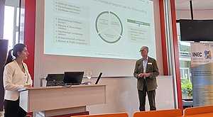 Professorin und Referent zeigen eine Präsentation.
